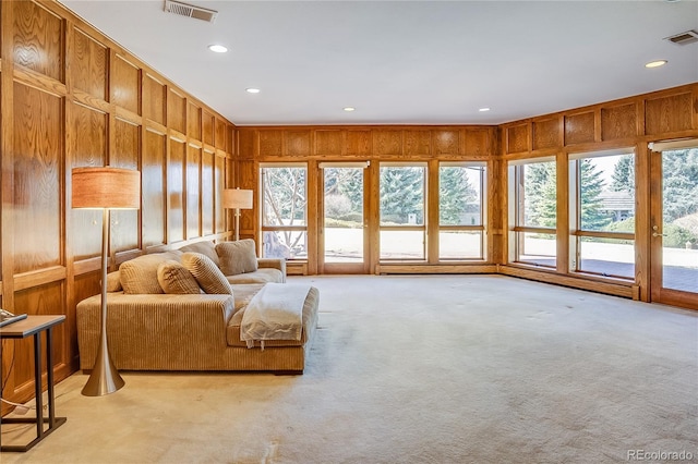 living room featuring wooden walls, visible vents, a wealth of natural light, and light carpet