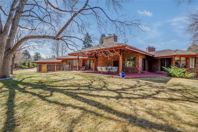 back of house featuring a patio, a yard, brick siding, and a chimney