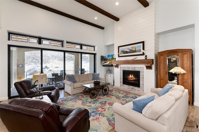 living room with beamed ceiling, light hardwood / wood-style flooring, a high ceiling, and a brick fireplace