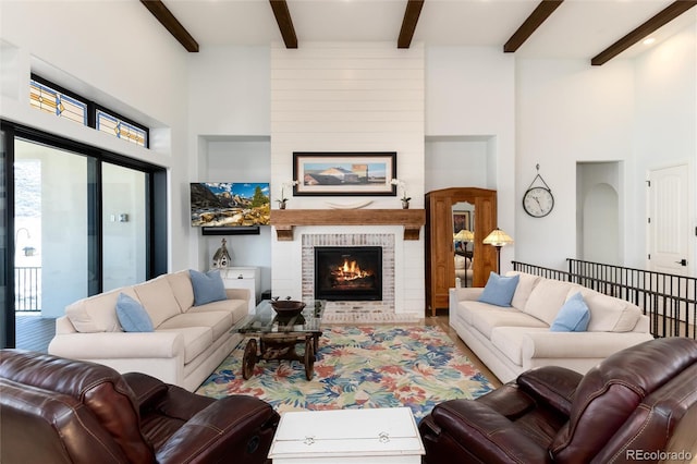 living room featuring plenty of natural light, beam ceiling, a towering ceiling, and a brick fireplace