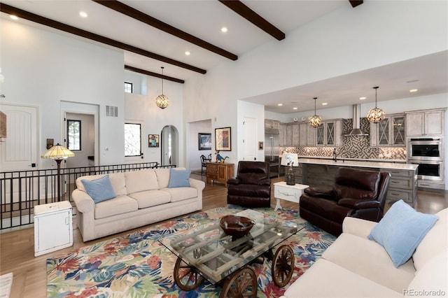 living room featuring beam ceiling, light wood-type flooring, sink, and a chandelier