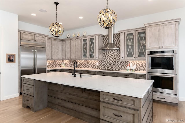 kitchen featuring appliances with stainless steel finishes, sink, hardwood / wood-style flooring, decorative light fixtures, and an island with sink