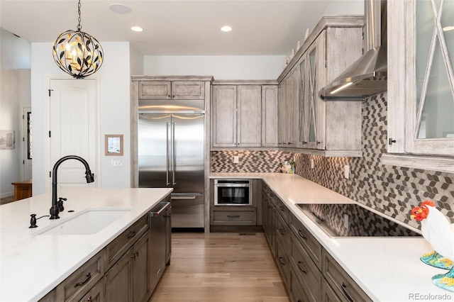 kitchen with sink, wall chimney range hood, pendant lighting, decorative backsplash, and appliances with stainless steel finishes