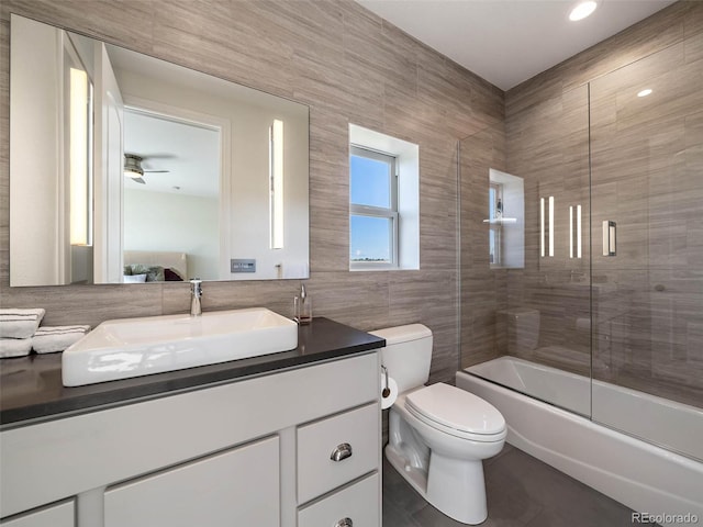 full bathroom featuring ceiling fan, combined bath / shower with glass door, tile walls, toilet, and vanity