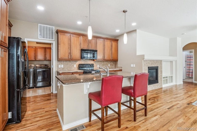 11972 W Long Cir Unit 104, Littleton, CO 80127 - kitchen featuring black appliances, washer and dryer, light wood-style flooring, brown cabinetry, and dark stone countertops