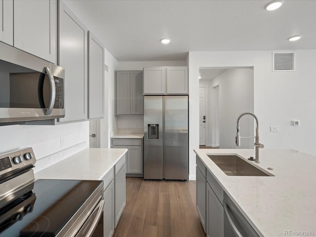 kitchen featuring sink, gray cabinets, stainless steel appliances, light stone counters, and dark hardwood / wood-style flooring