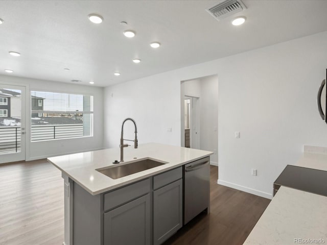 kitchen featuring dishwasher, sink, gray cabinetry, hardwood / wood-style flooring, and a kitchen island with sink