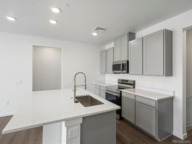 kitchen featuring sink, appliances with stainless steel finishes, gray cabinets, light stone countertops, and a kitchen island with sink