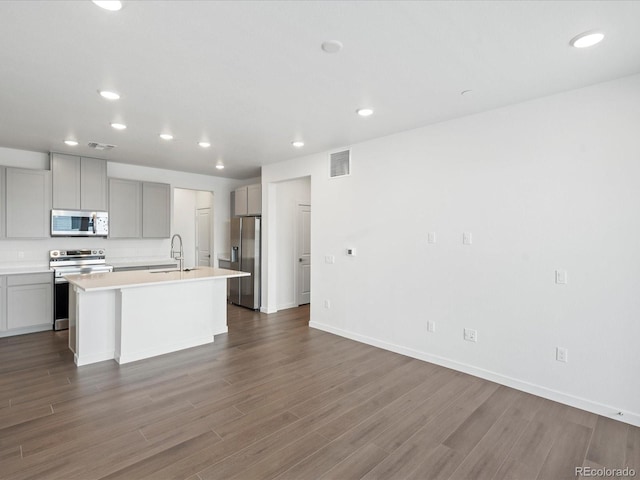 kitchen featuring sink, gray cabinets, appliances with stainless steel finishes, a center island with sink, and dark hardwood / wood-style flooring