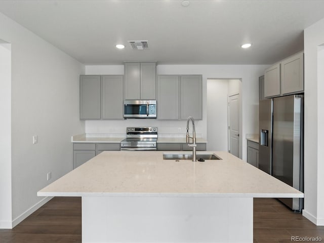 kitchen featuring an island with sink, appliances with stainless steel finishes, gray cabinets, and sink