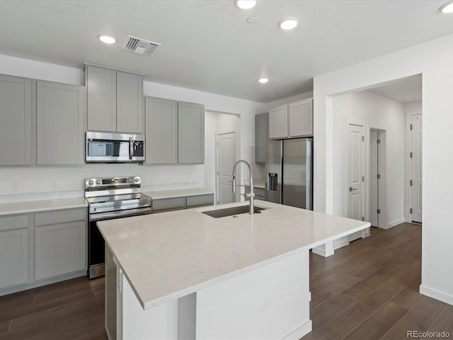 kitchen featuring dark hardwood / wood-style floors, sink, stainless steel appliances, light stone countertops, and a center island with sink