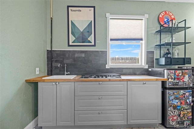 kitchen featuring freestanding refrigerator, white cabinetry, a sink, wood counters, and stainless steel gas stovetop