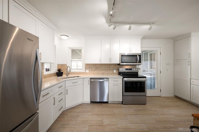 kitchen with stainless steel appliances, a sink, white cabinets, light countertops, and tasteful backsplash