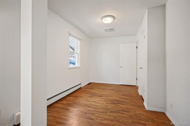 empty room with a baseboard heating unit, wood finished floors, and baseboards