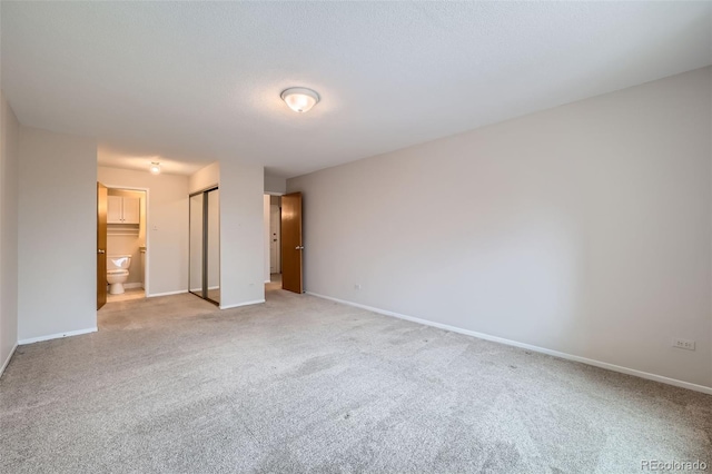 unfurnished bedroom with ensuite bath, a closet, and light carpet