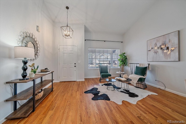 sitting room with a chandelier, high vaulted ceiling, baseboards, and wood finished floors