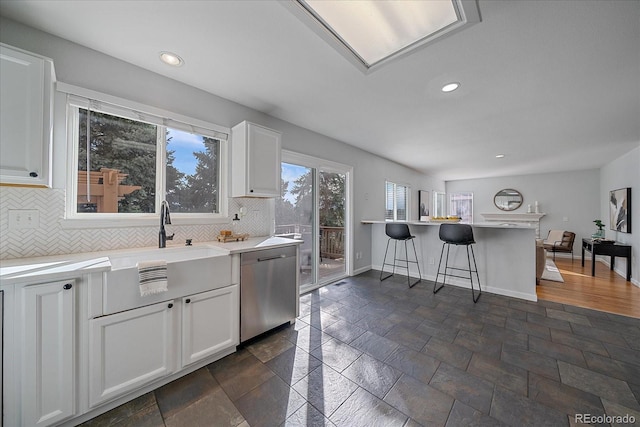 kitchen featuring baseboards, white cabinets, dishwasher, a breakfast bar area, and backsplash