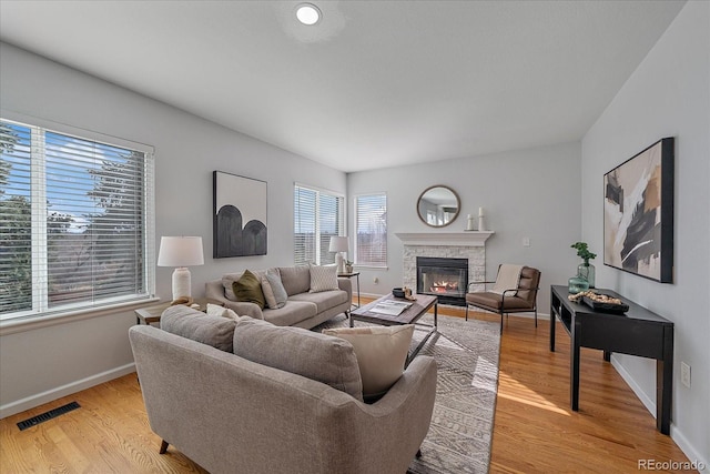 living area with light wood finished floors, a fireplace, visible vents, and baseboards