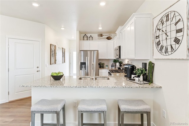 kitchen featuring kitchen peninsula, appliances with stainless steel finishes, a kitchen bar, and white cabinets