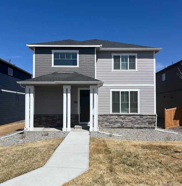 view of front of home featuring stone siding, a shingled roof, and a front lawn