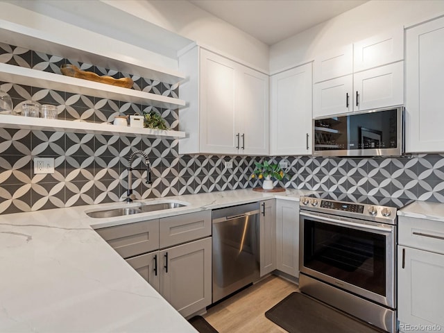 kitchen featuring a sink, open shelves, stainless steel appliances, decorative backsplash, and light stone counters