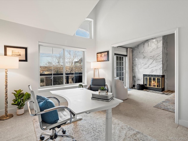 office space featuring baseboards, a fireplace, carpet floors, and a towering ceiling