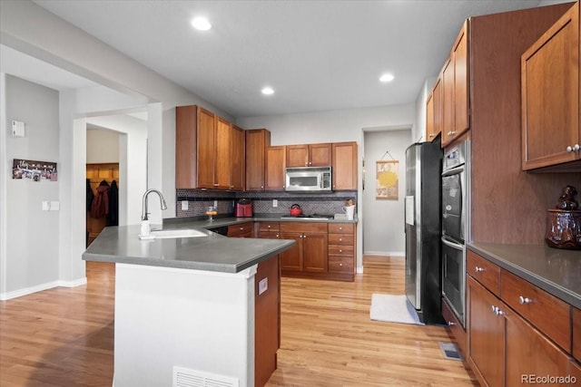 kitchen with sink, appliances with stainless steel finishes, tasteful backsplash, light hardwood / wood-style floors, and kitchen peninsula