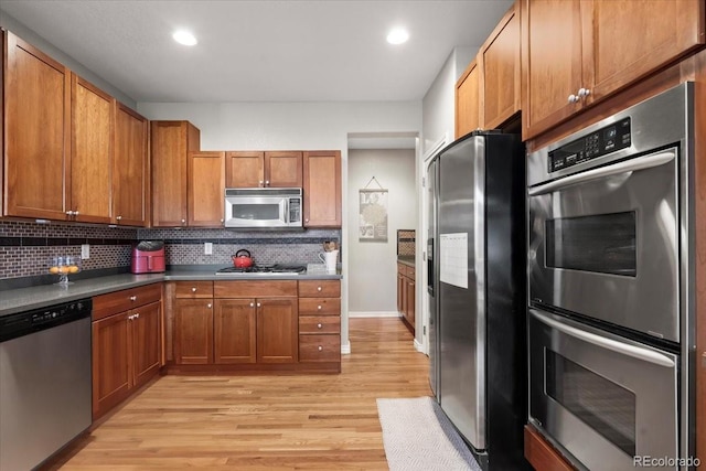 kitchen with backsplash, appliances with stainless steel finishes, and light hardwood / wood-style flooring