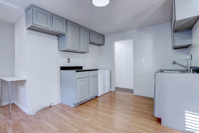 kitchen featuring tasteful backsplash, light hardwood / wood-style floors, gray cabinetry, and sink