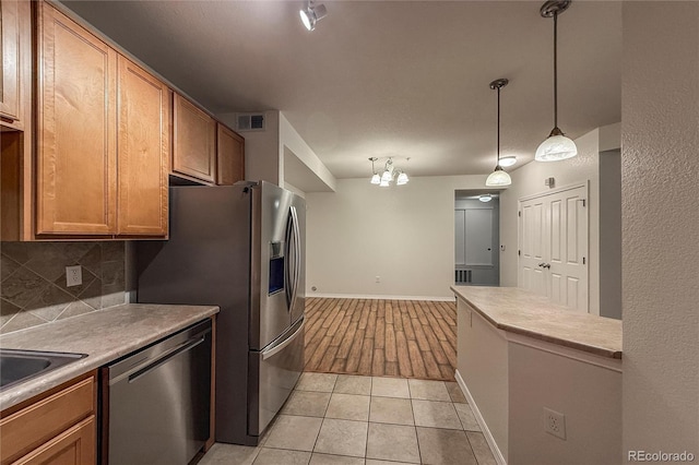804 Summer Hawk Dr Unit 5105, Longmont, CO 80504 - kitchen featuring stainless steel appliances, backsplash, light countertops, a chandelier, and brown cabinetry