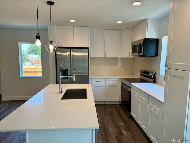 kitchen with appliances with stainless steel finishes, white cabinetry, decorative backsplash, decorative light fixtures, and a center island with sink