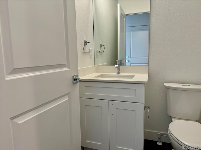 bathroom featuring toilet, vanity, and a textured wall