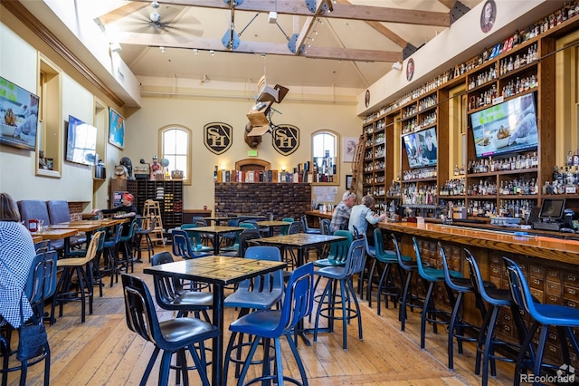 bar with hardwood / wood-style floors, a community bar, and vaulted ceiling with beams