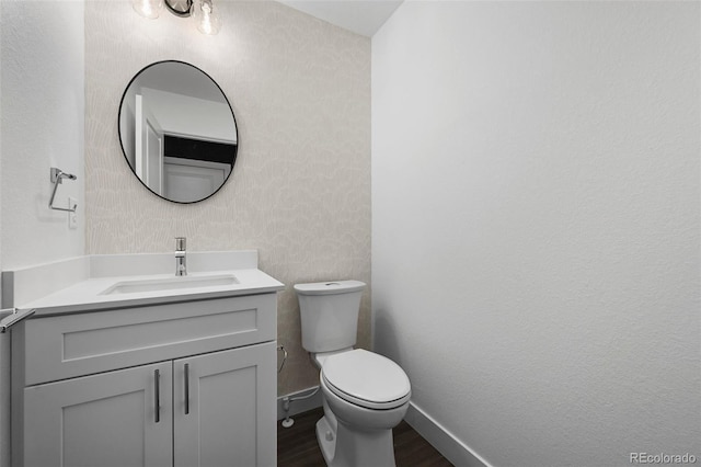 half bath featuring toilet, baseboards, wood finished floors, and vanity
