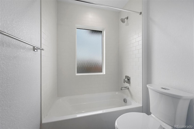 bathroom with toilet, shower / tub combination, and a textured wall