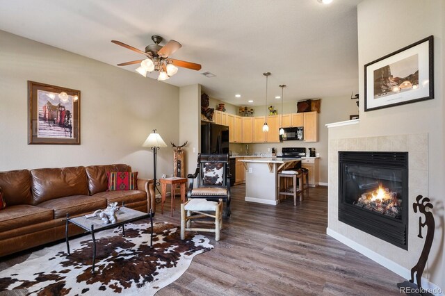 living room featuring hardwood / wood-style flooring, a tile fireplace, and ceiling fan