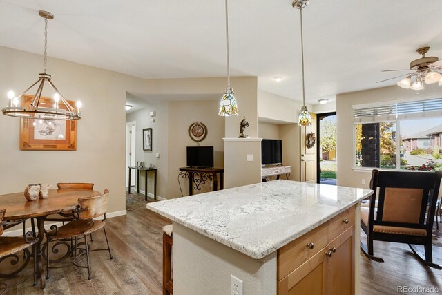 kitchen with light stone counters, hanging light fixtures, a center island, and hardwood / wood-style flooring