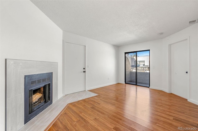 unfurnished living room with baseboards, visible vents, light wood-style flooring, a textured ceiling, and a fireplace