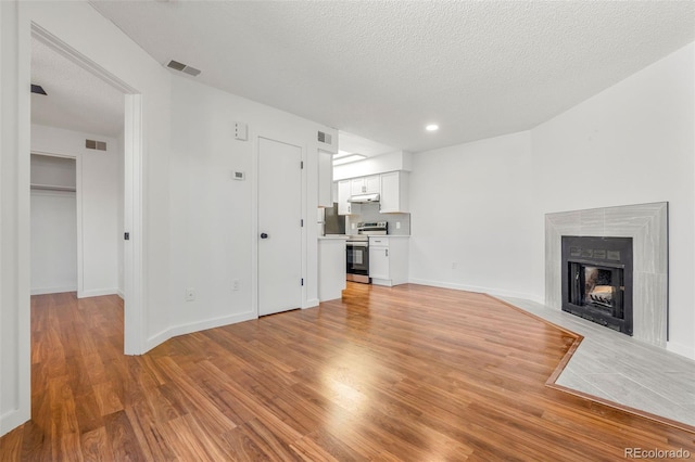 unfurnished living room featuring a fireplace with flush hearth, visible vents, and light wood finished floors