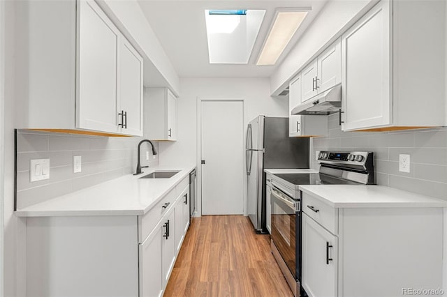 kitchen featuring a skylight, light wood finished floors, appliances with stainless steel finishes, a sink, and under cabinet range hood