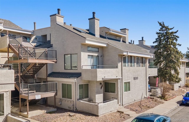 rear view of property with a shingled roof and stucco siding