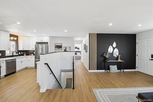 kitchen with stainless steel appliances, light wood-style floors, white cabinets, a center island, and tasteful backsplash