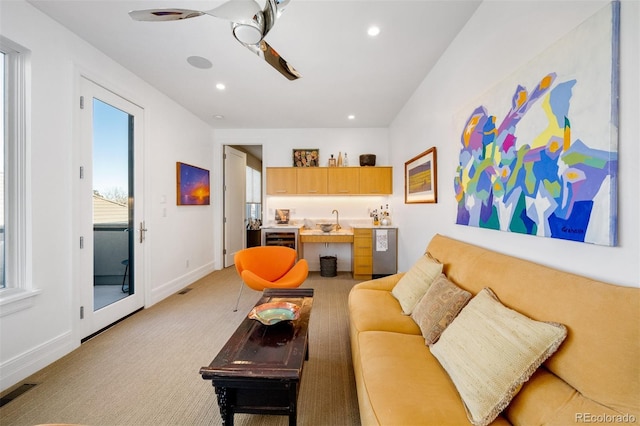 living room featuring wine cooler, light colored carpet, ceiling fan, and bar area