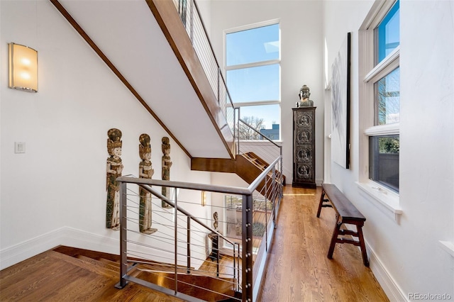 stairs with wood finished floors, baseboards, plenty of natural light, and a towering ceiling