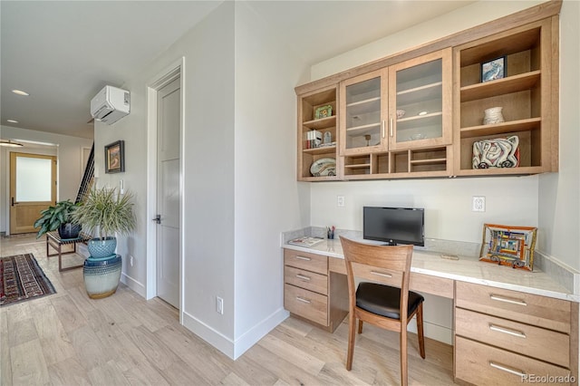 home office with light wood-style floors, baseboards, a wall unit AC, and built in desk
