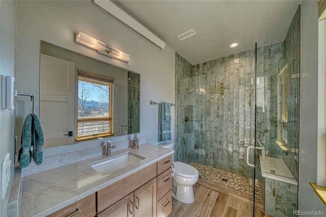 bathroom with vanity, toilet, a shower stall, wood finished floors, and visible vents