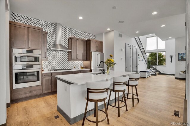 21345 E 59th Dr, Aurora, CO 80019 - kitchen featuring stainless steel appliances, wall chimney range hood, a center island with sink, light countertops, and a kitchen bar