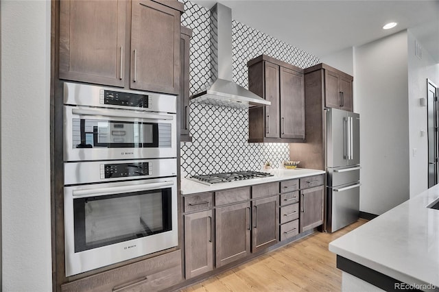 21345 E 59th Dr, Aurora, CO 80019 - kitchen featuring stainless steel appliances, wall chimney range hood, light countertops, light wood-style flooring, and decorative backsplash