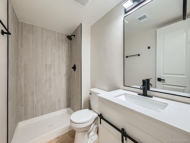 full bathroom with visible vents, a textured wall, toilet, a tile shower, and vanity