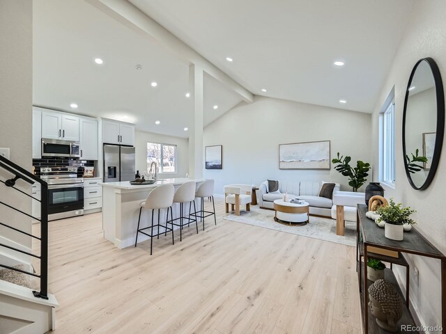 kitchen featuring a breakfast bar, vaulted ceiling with beams, stainless steel appliances, light countertops, and light wood-type flooring